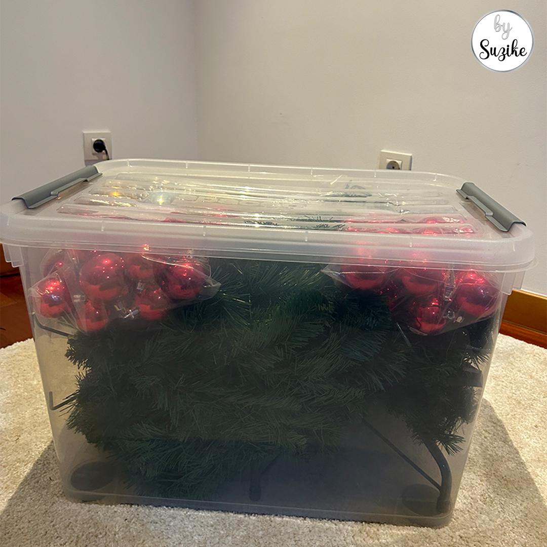 Large plastic storage box filled with Christmas tree branches and red baubles.