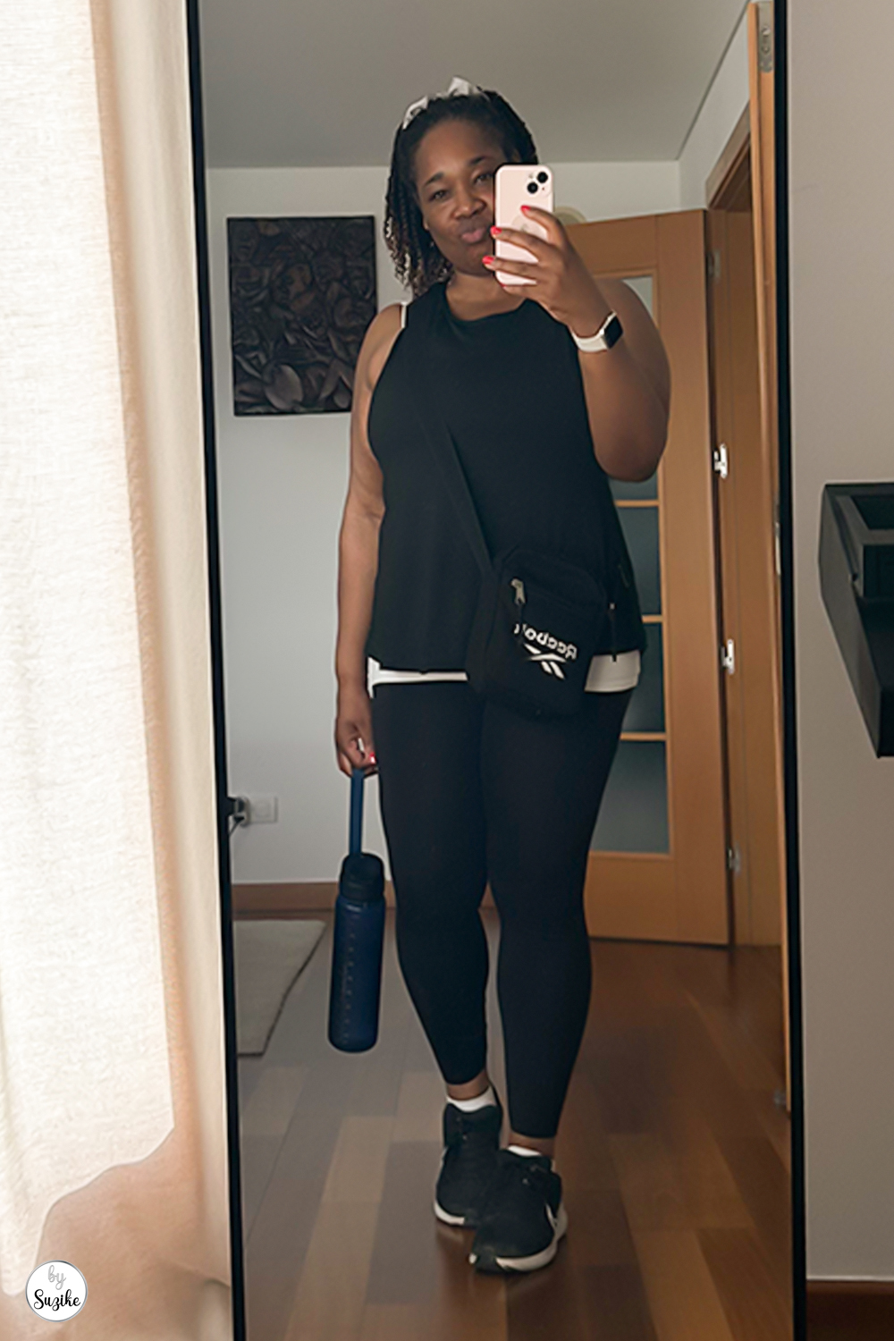 Full-body mirror selfie of Suzike in black workout clothes, holding a blue water bottle, ready for a power walk.