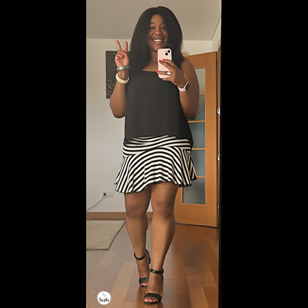 Woman wearing a black sleeveless top and black-and-white striped mini skirt, smiling and making a peace sign in a stylish summer outfit.