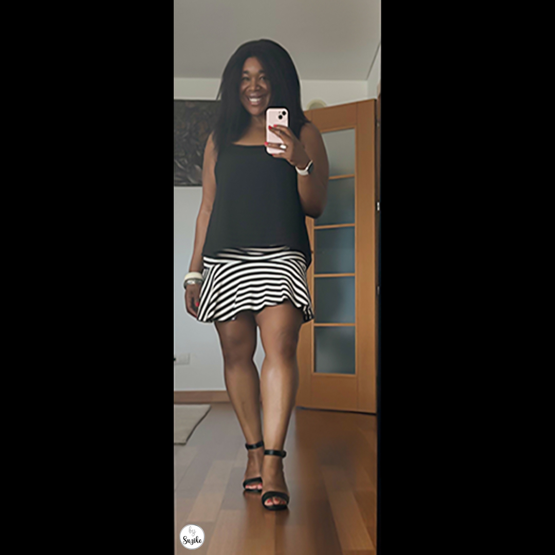 Full-body shot of a woman in a black sleeveless top and striped mini skirt, showing a chic and comfortable summer look with black sandals.