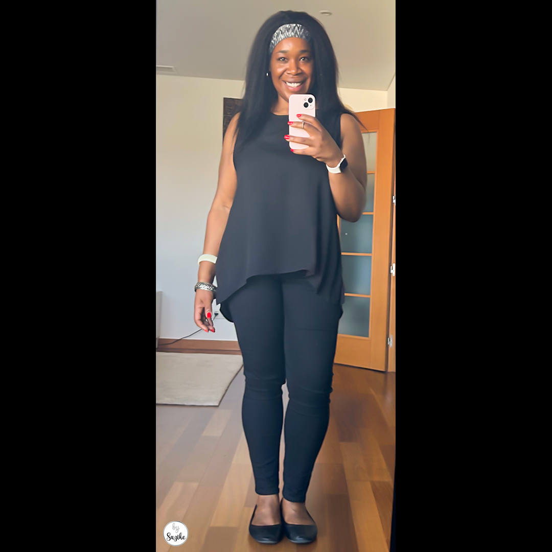 Woman wearing a black sleeveless top and black skinny jeans, smiling and holding a phone, showcasing a simple all-black outfit.