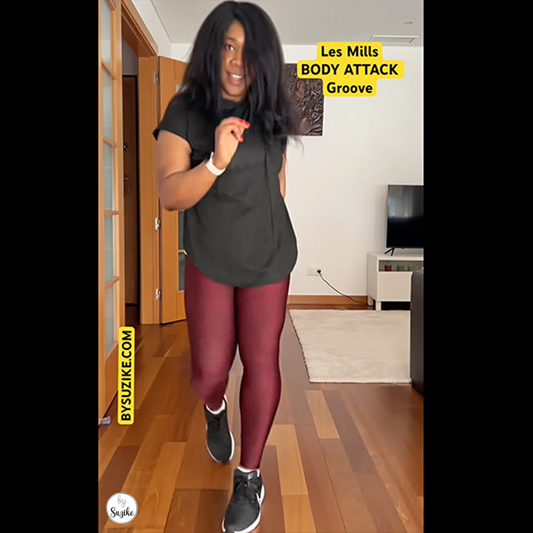 Woman in black workout clothes smiling and moving energetically at home, mid-groove, with “Les Mills BodyAttack Groove” text on screen.