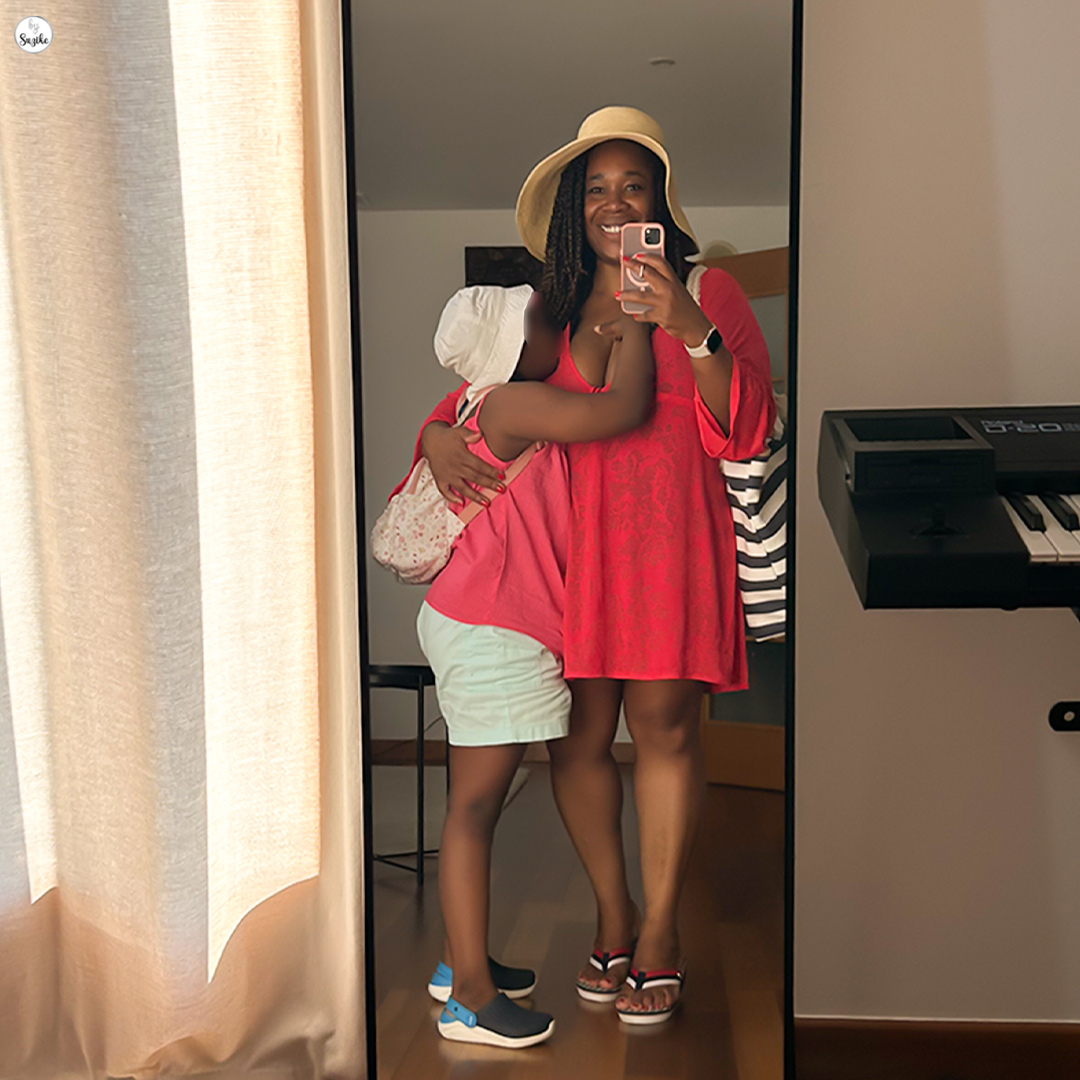 Mom and daughter showing their beach outfits before a beach day with kids, hugging in front of a mirror with a striped beach bag.