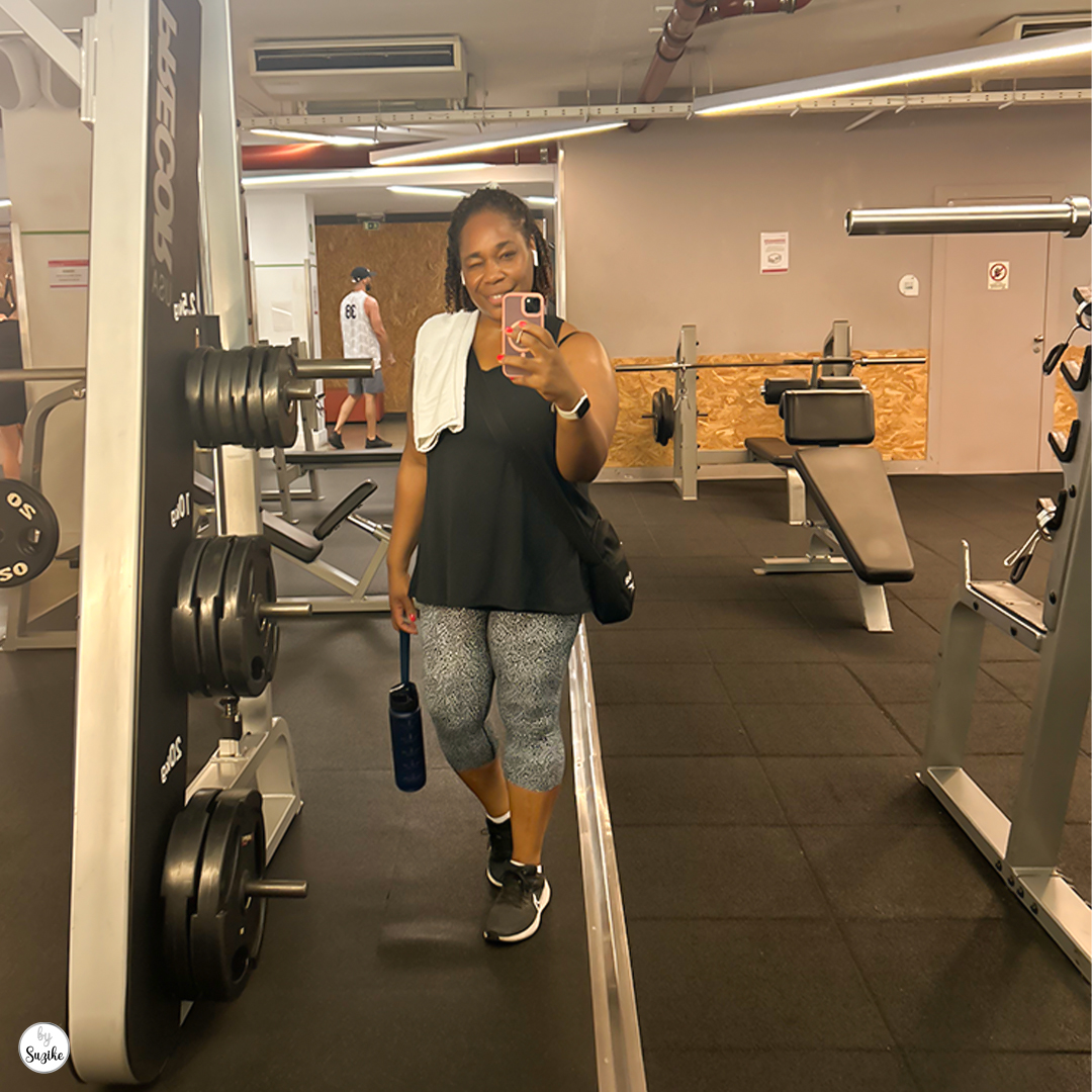 Woman smiling in gym clothes, holding a water bottle, stands in front of gym equipment at Solinca Light Alvalade, Lisbon.