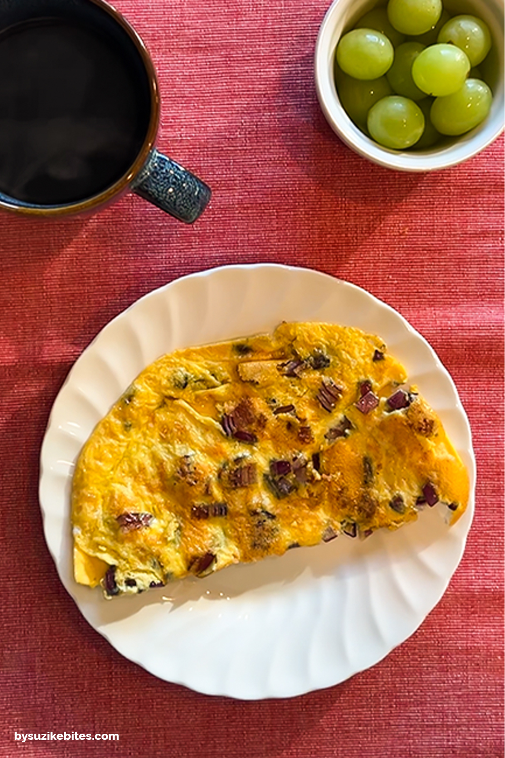 Day 8 breakfast of my weight loss journey: omelette with onions and herbs, green grapes and black coffee on a red tablecloth