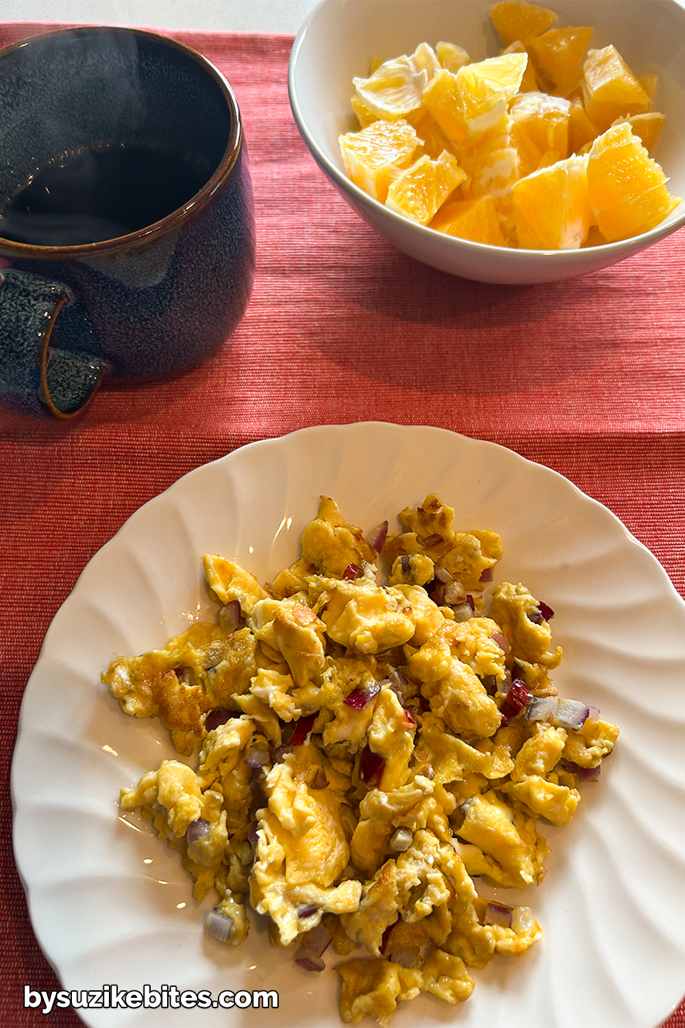 Healthy low carb breakfast with scrambled eggs, fresh orange and black coffee on a red tablecloth – part of my weight loss journey.
