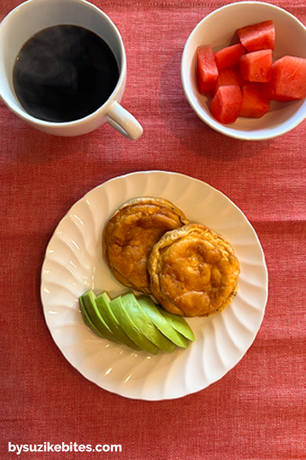 Healthy breakfast from my weight loss journey featuring egg muffins with avocado slices, watermelon cubes, and black coffee on a red tablecloth.