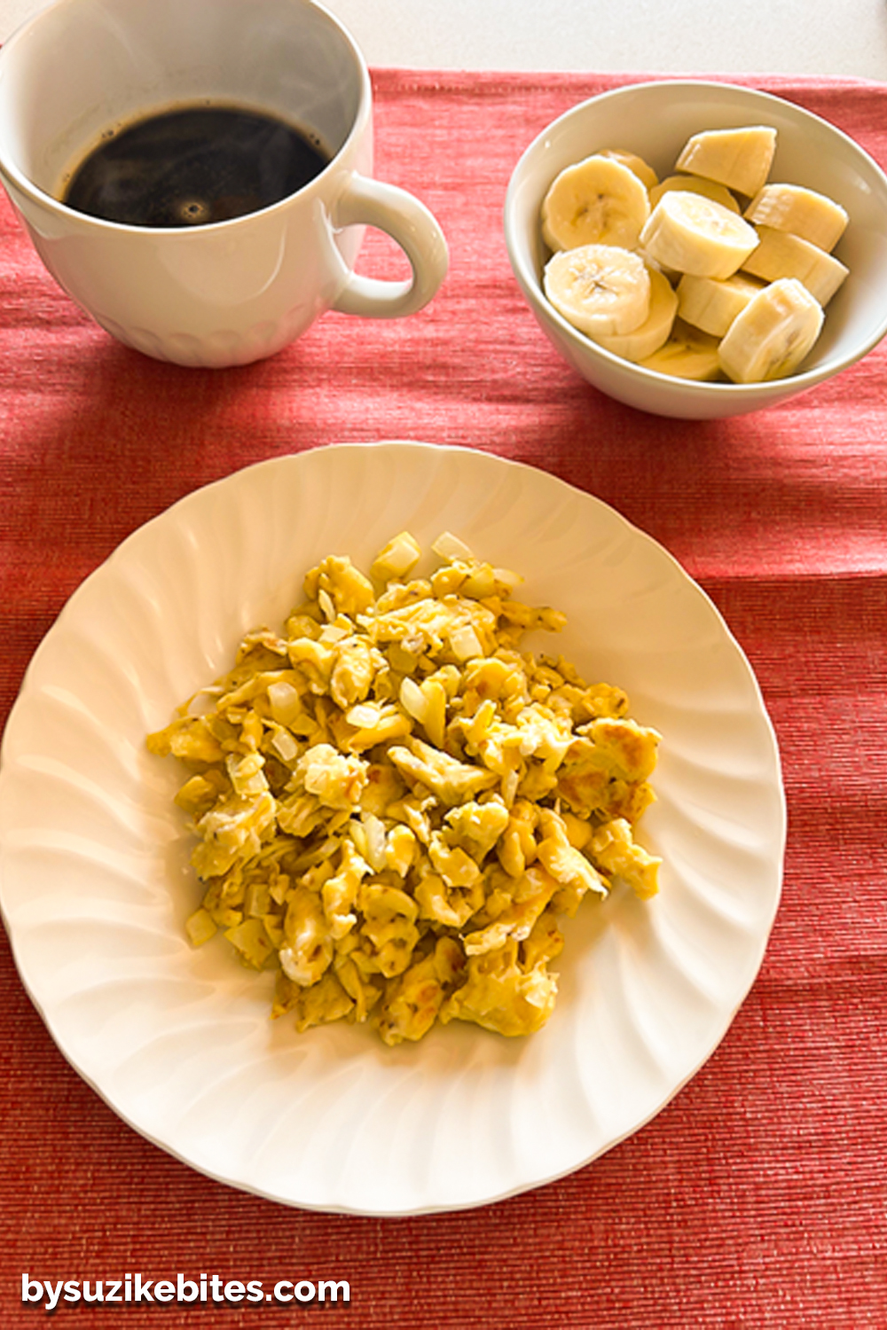 Healthy breakfast of scrambled eggs served with sliced banana and black coffee on a red placemat, part of a balanced weight loss journey meal.