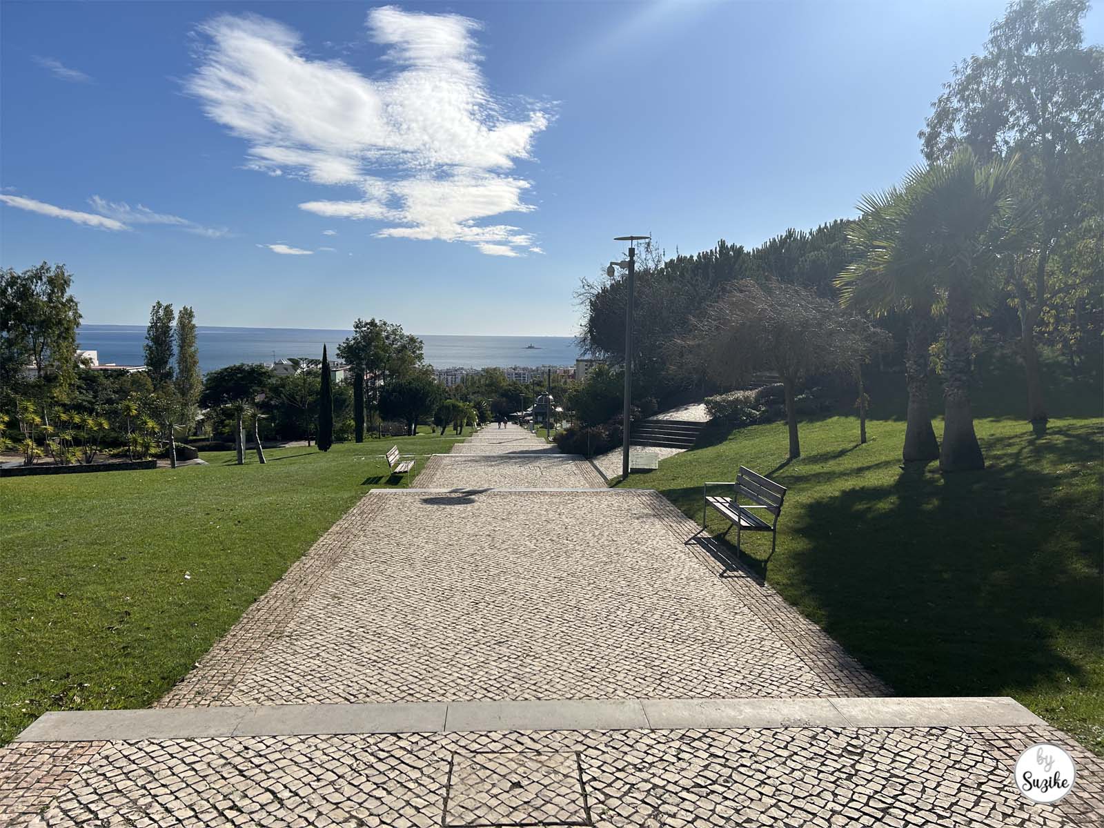 Wide cobblestone path leading downhill with sea views at the Park of the Poets in Oeiras