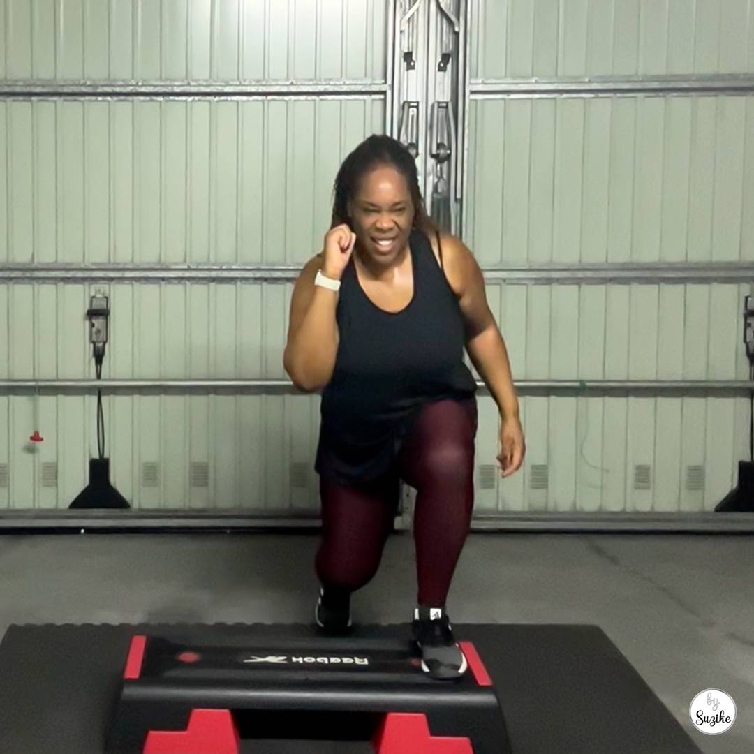 Suzike doing a Body Step workout on Day 28 of her Dream Pyramid weight loss journey, stepping forward in a lunge while smiling during her home gym session.