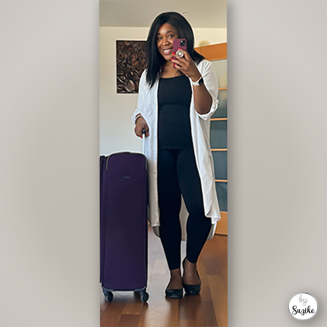 woman wearing the best travel outfit for women with a white cardigan, black top, black leggings and a purple suitcase