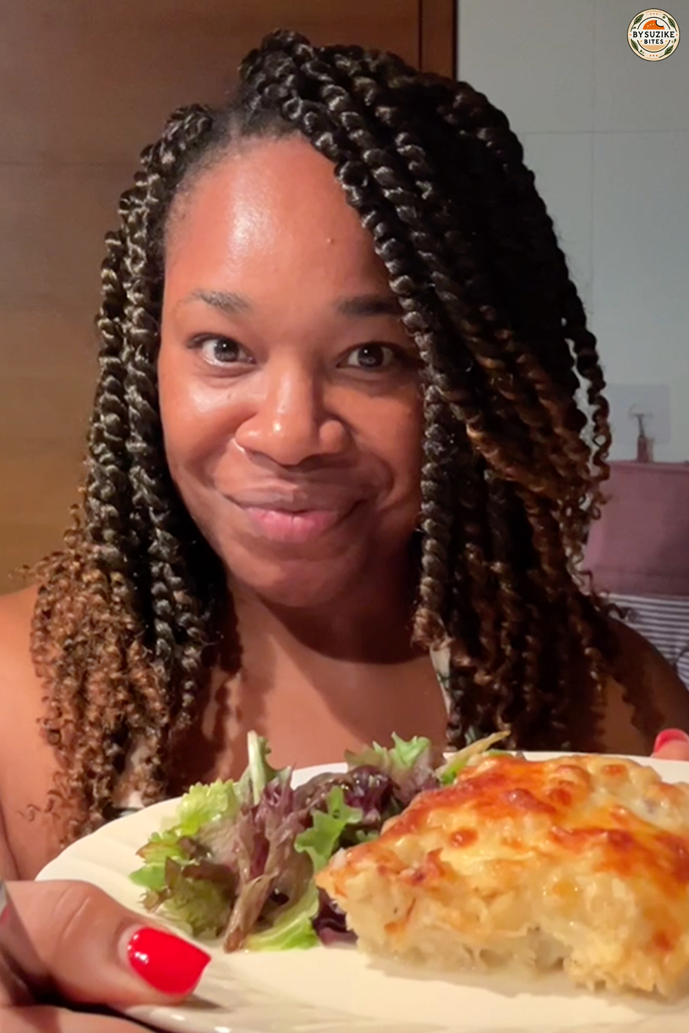 Suzike holding a plate with a homemade meal and salad, smiling in the kitchen.