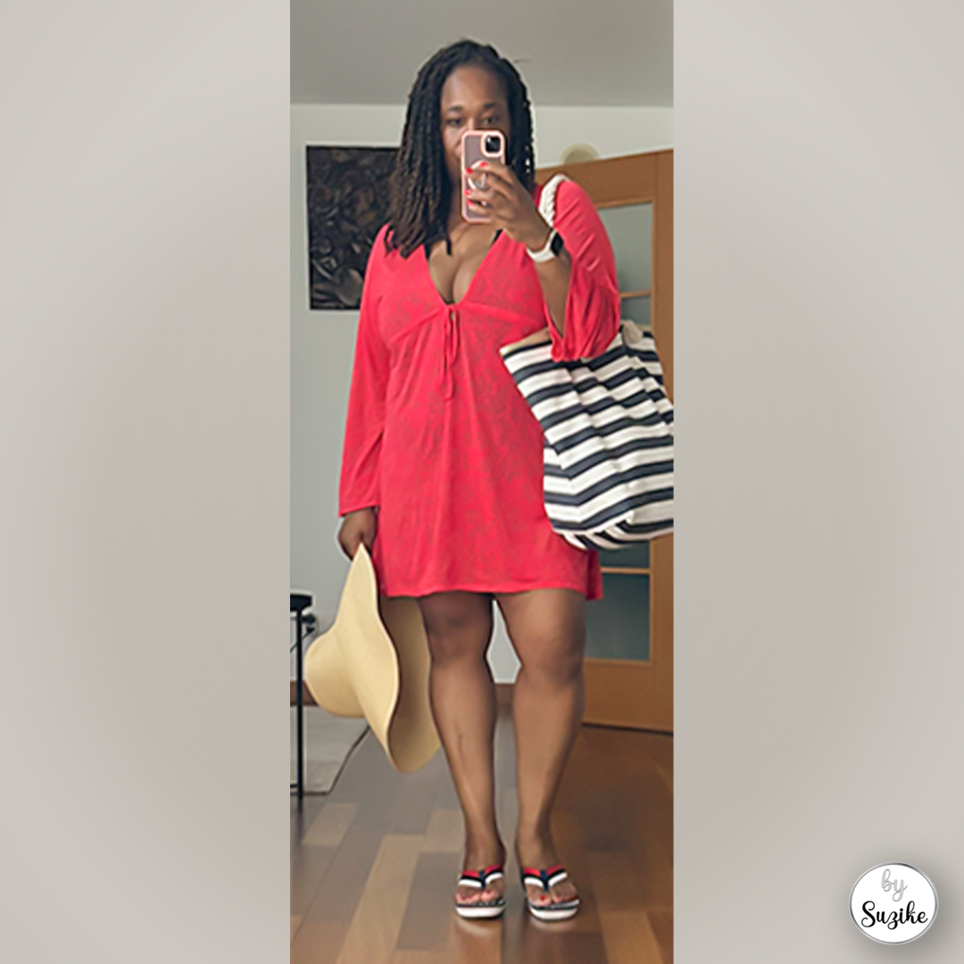 Mirror selfie of Suzike holding a beach hat while wearing a red summer dress and striped tote bag, casual summer outfit look.