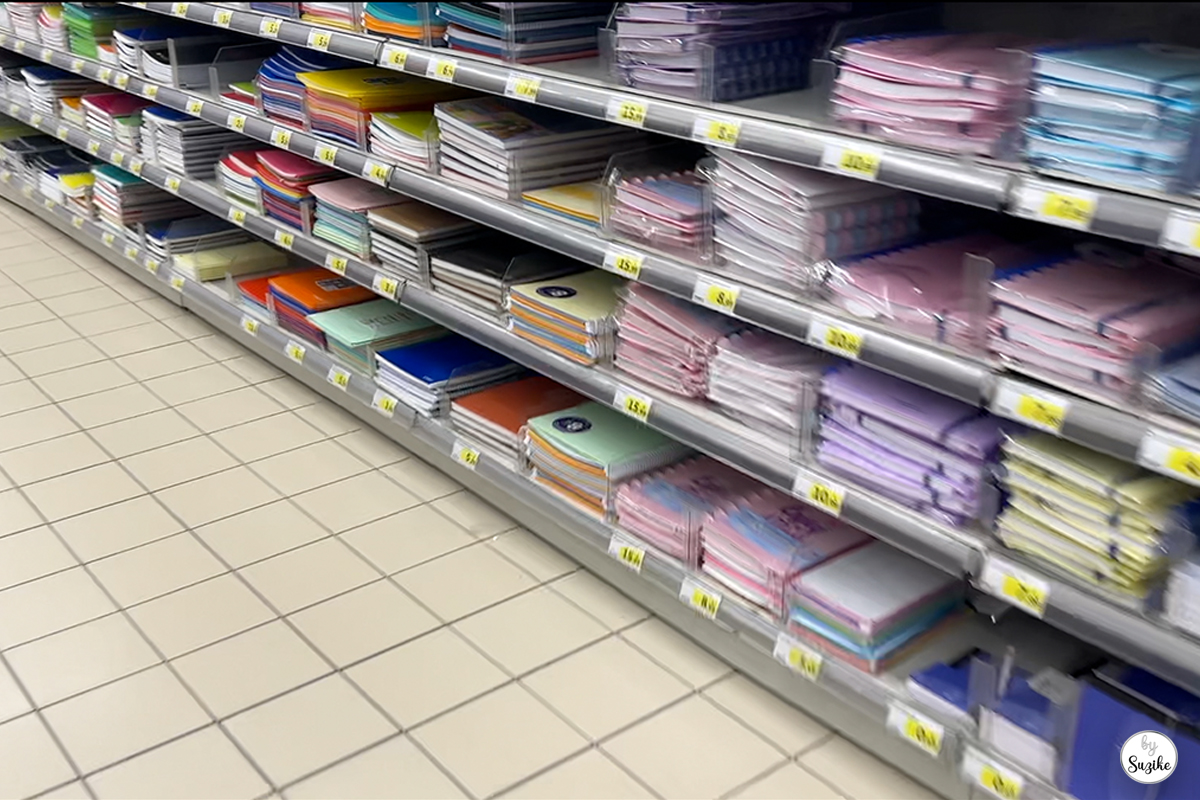 Supermarket aisle with shelves full of notebooks and school supplies during Suzike’s quick grocery run.