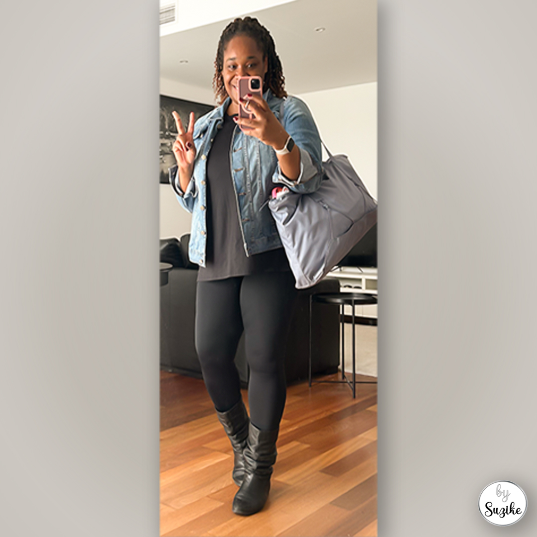 Woman wearing a denim jacket, black top, black leggings and black boots, holding a large grey tote bag while posing for a mirror selfie.