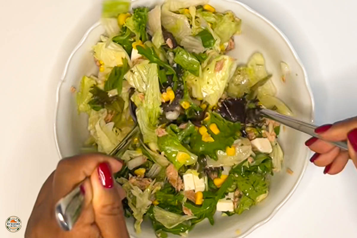 Tossing a 10-minute feta and tuna salad in a bowl with lettuce, feta, corn, and tuna before serving