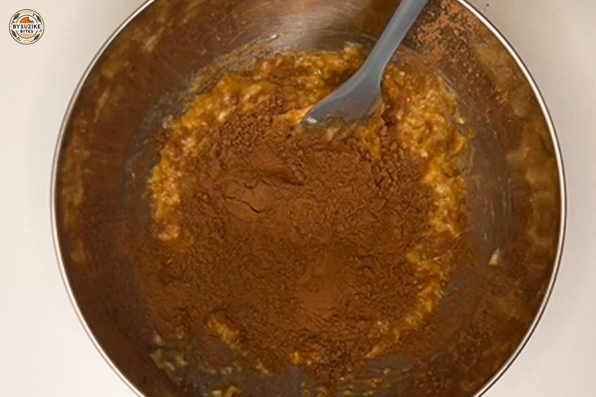 Cocoa powder added to banana and peanut butter mixture in a bowl.