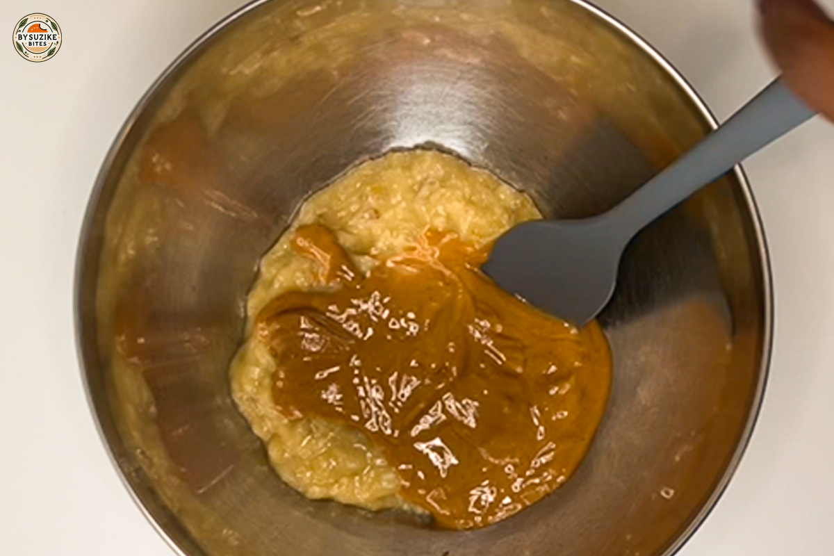 Peanut butter added to mashed bananas in a mixing bowl.