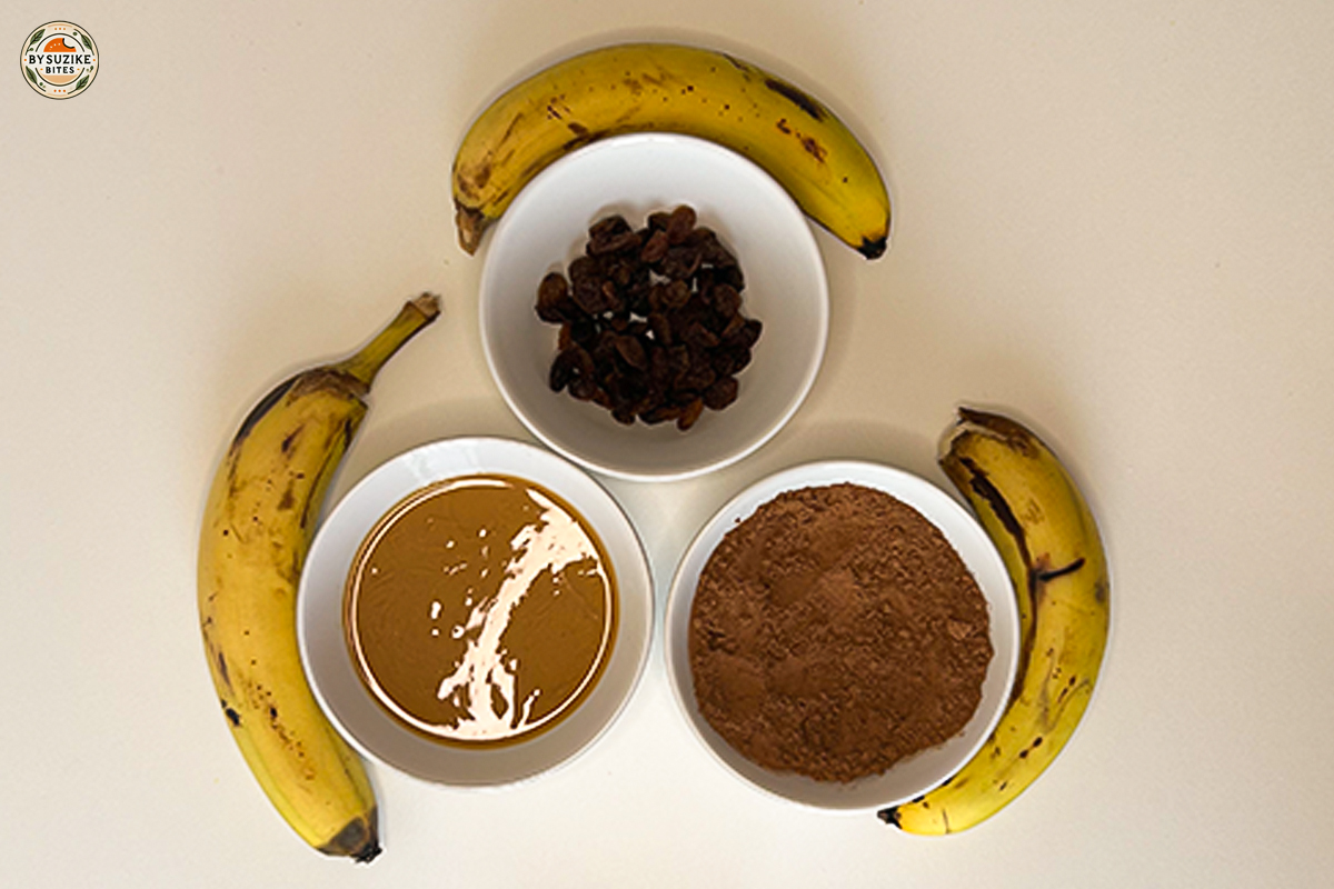 Banana brownie ingredients arranged on a white background (bananas, peanut butter, cocoa, and raisins).