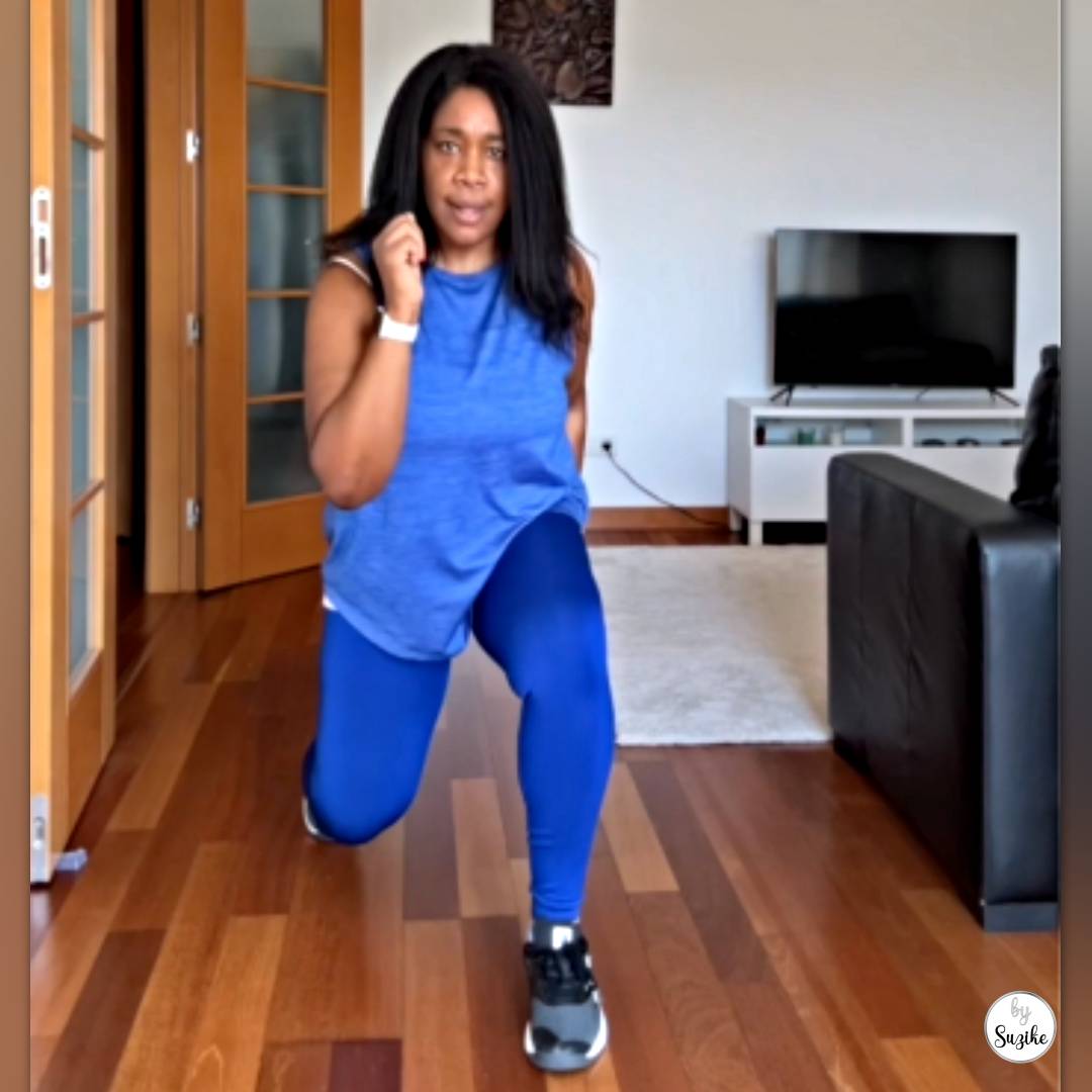 Woman holding a forward lunge at home on a wooden floor, wearing a blue workout outfit and trainers.