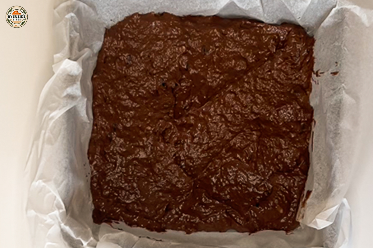 Vegan banana brownie batter spread in a parchment-lined baking pan.