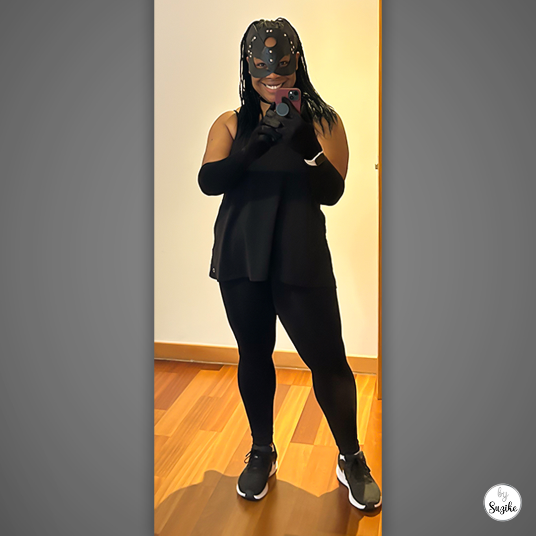 Catwoman costume for women wearing a black cat mask and long black gloves with an all-black outfit and trainers, standing indoors.