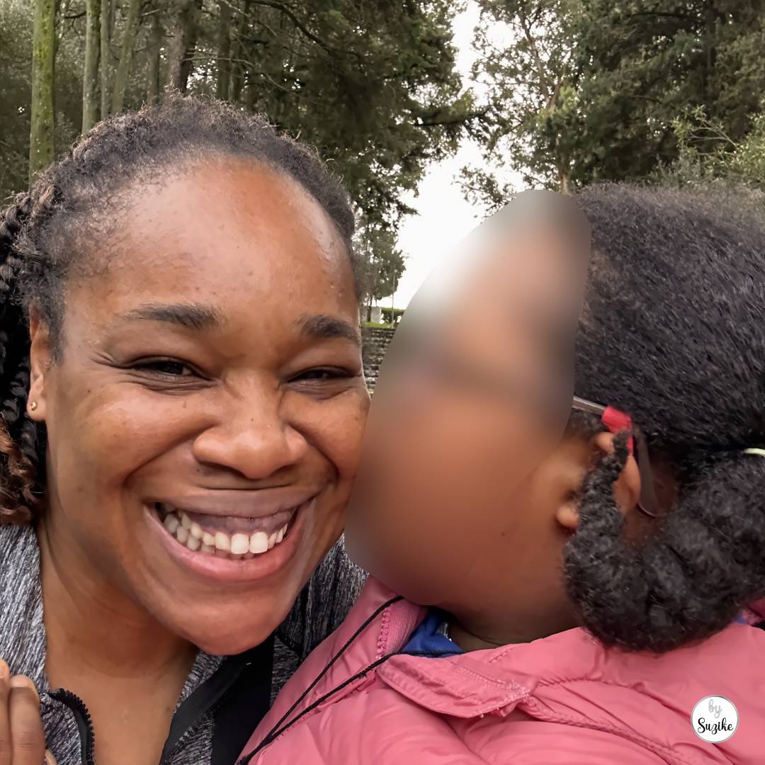 Felisberta kissing Suzike on the cheek during a cold morning walk, with stone steps and trees behind them.