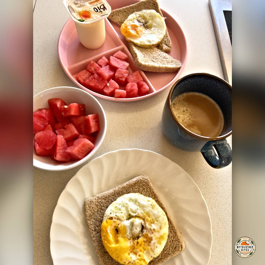Egg on whole wheat toast served with watermelon cubes, a yogurt cup, and a cup of coffee on a kitchen counter.