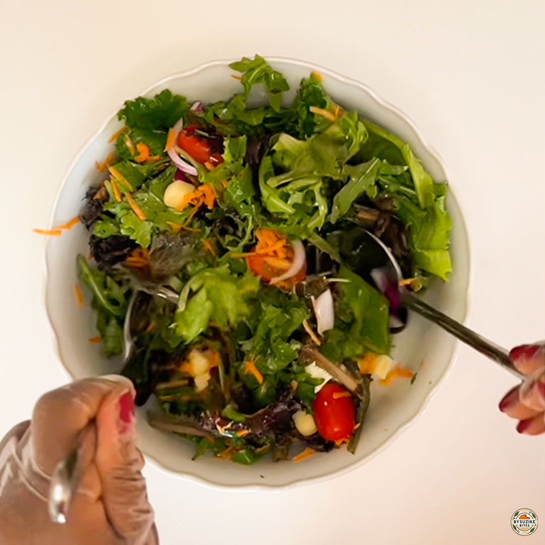 Egg salad with feta and mozzarella in a bowl, mixed greens with cherry tomatoes and vinaigrette being tossed.