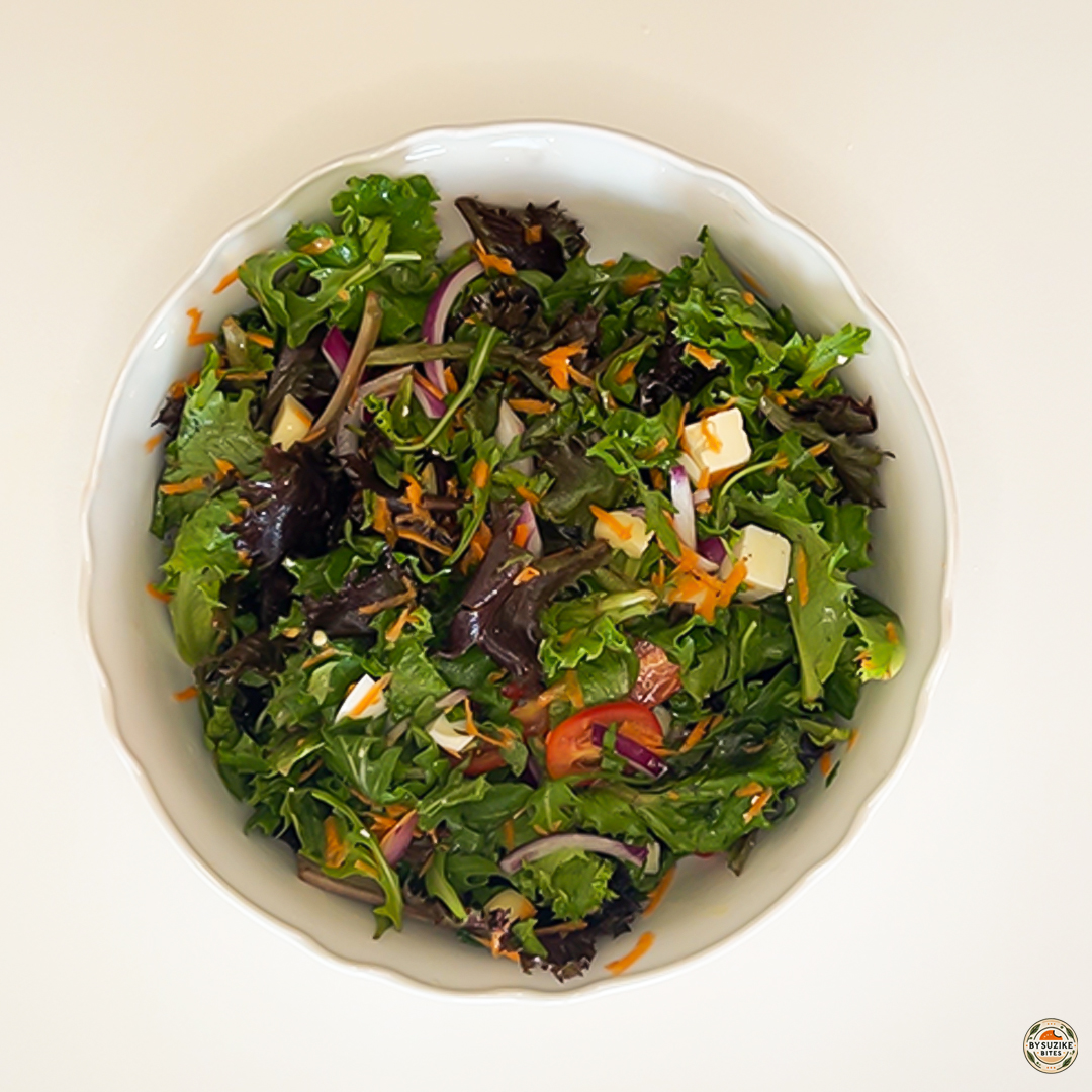 Egg salad with feta and mozzarella in a white bowl with mixed greens, red onion, shredded carrot, cherry tomatoes, and cheese cubes.