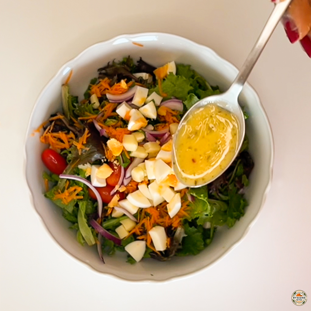 Egg salad with feta and mozzarella being finished with a vinaigrette drizzle in a white bowl.