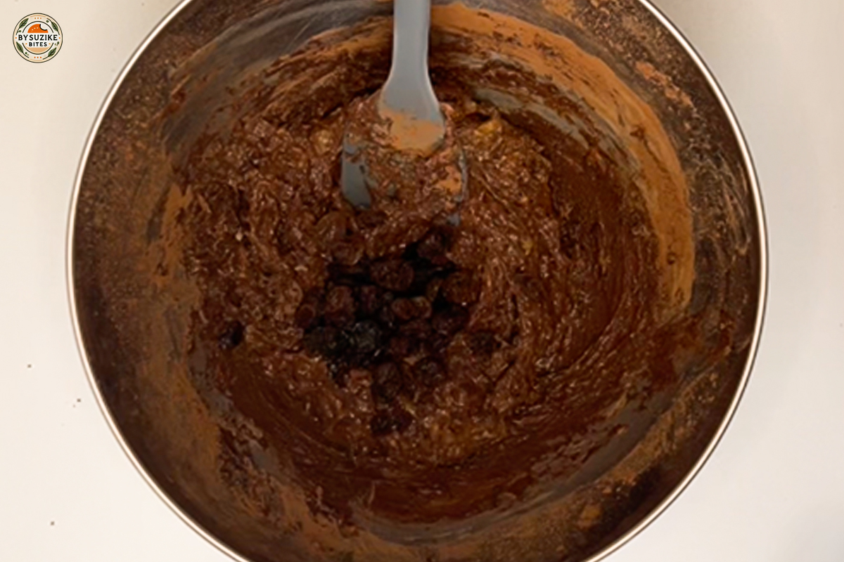 Cocoa powder added to banana and peanut butter mixture in a bowl.
