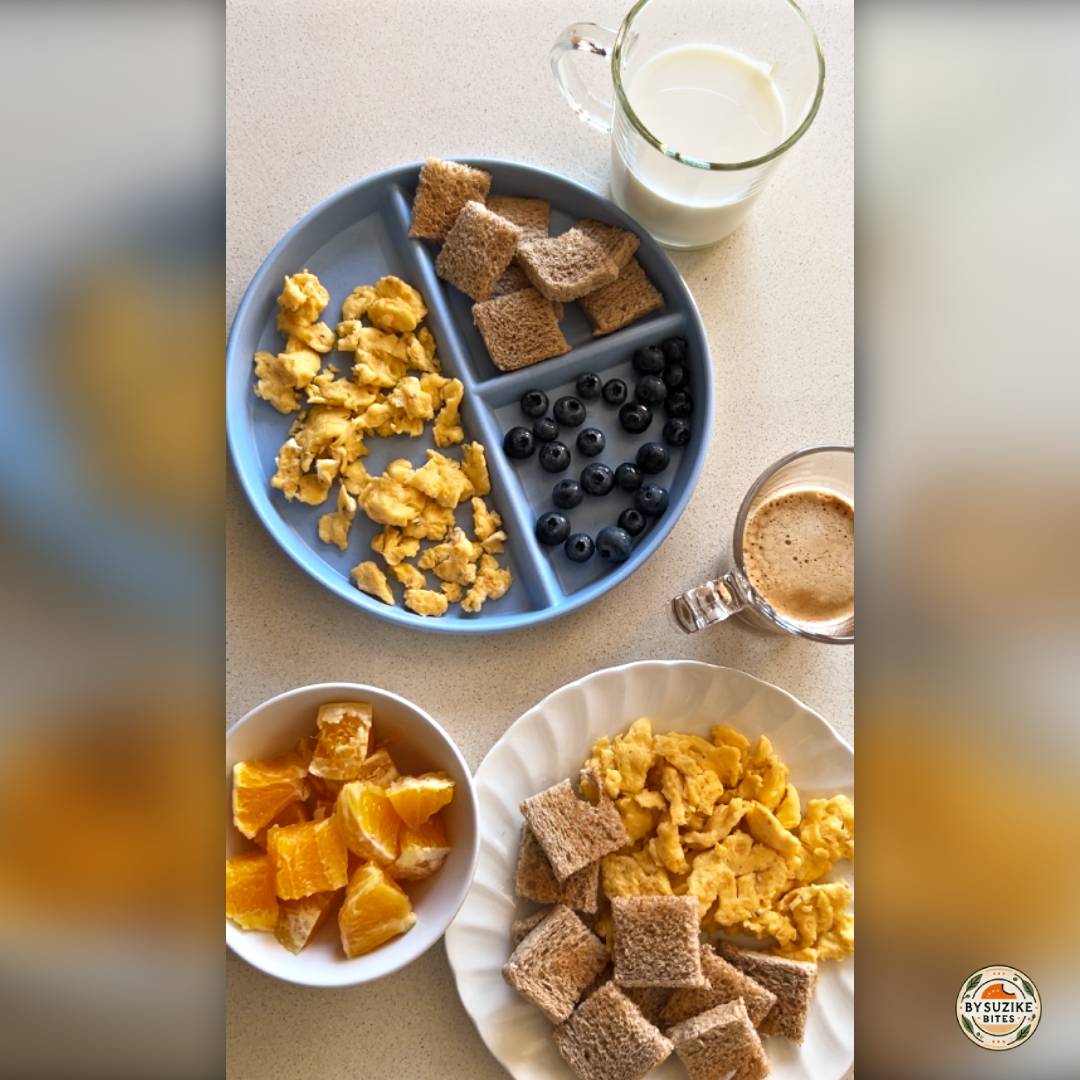 Mom and daughter scrambled eggs breakfast with toast squares, blueberries, orange pieces, a glass of milk, and a cup of coffee on a kitchen counter.