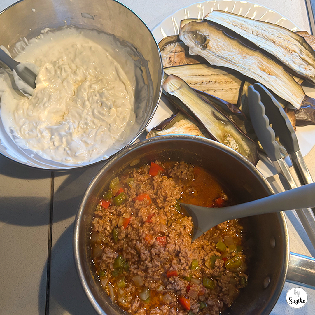 silicone cooking utensils review showing a light blue cooking spoon stirring ground meat sauce in a pot with grilled eggplant and yogurt sauce on the side