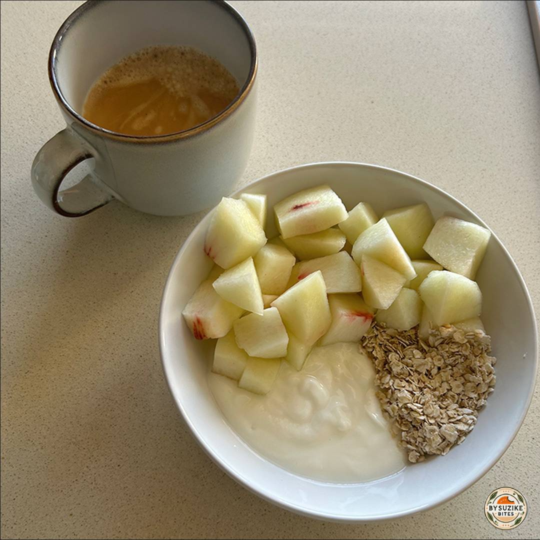 Bowl with yogurt, rolled oats, and chopped nectarine served with a cup of coffee on a kitchen counter.