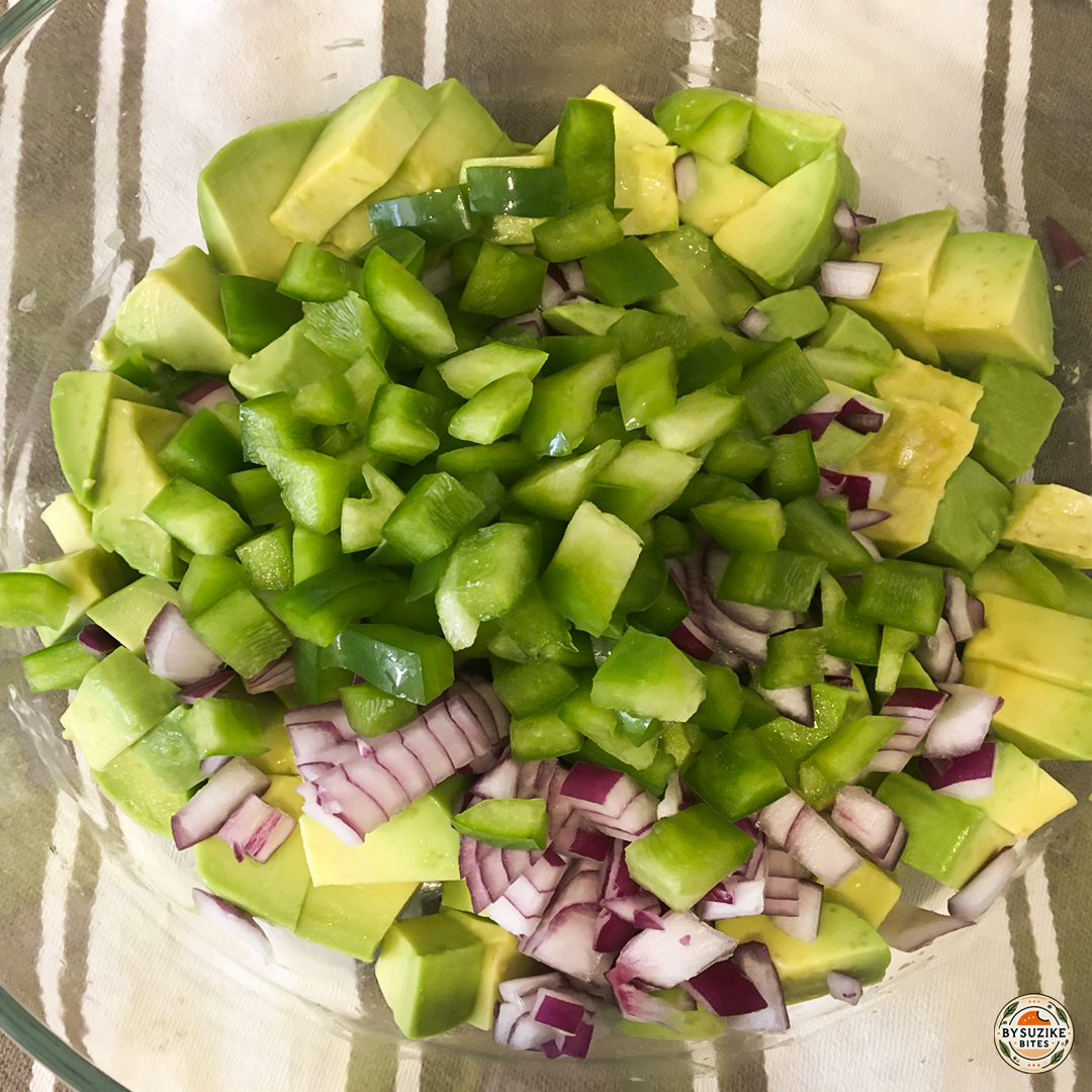 Chopped green pepper added to avocado and red onion in a bowl.