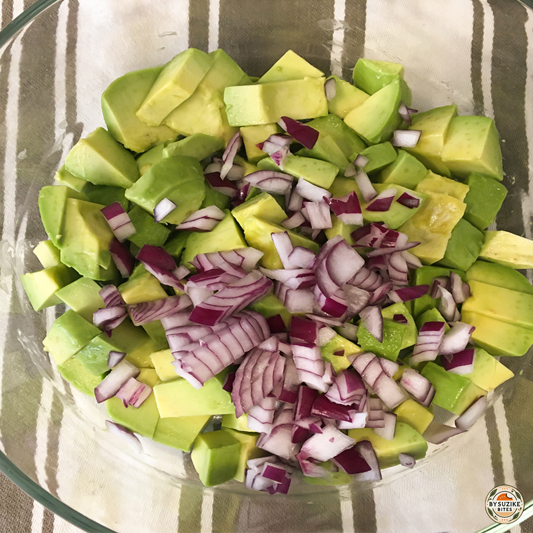 Red onion added to chopped avocado in a bowl for avocado salad.