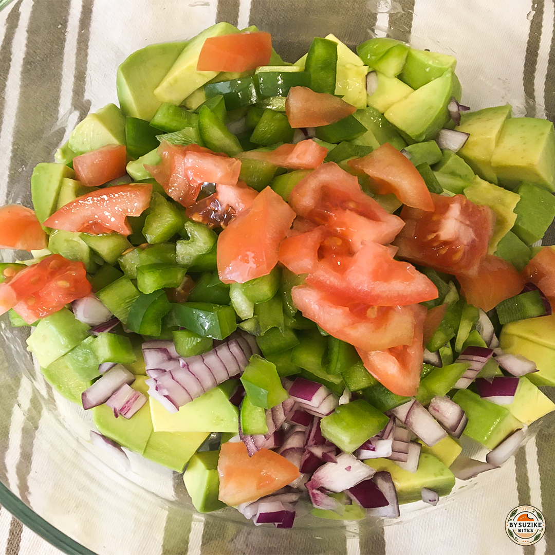 Tomato added to avocado, green pepper and red onion in a bowl.