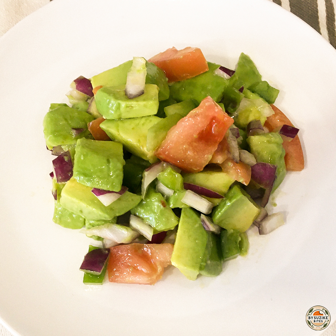 Avocado salad served on a white plate with tomato, green pepper and red onion.