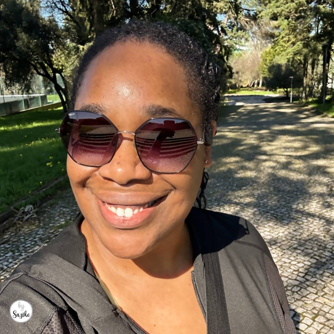 Smiling woman wearing sunglasses taking a sunny outdoor selfie on a tree-lined path during a weekend walk in Lisbon.
