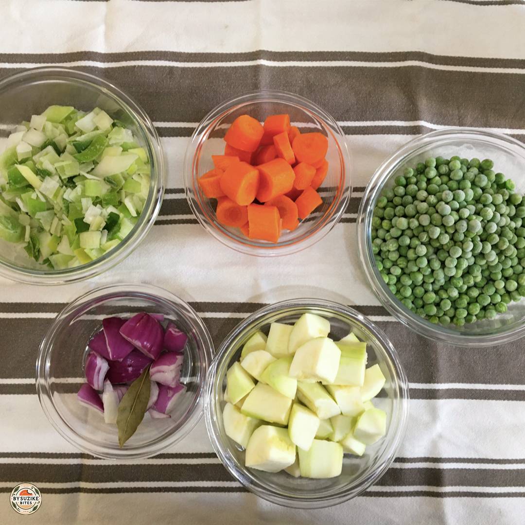 Bowls of chopped leeks, carrots, frozen peas, red onion, and zucchini prepared for creamy pea soup.