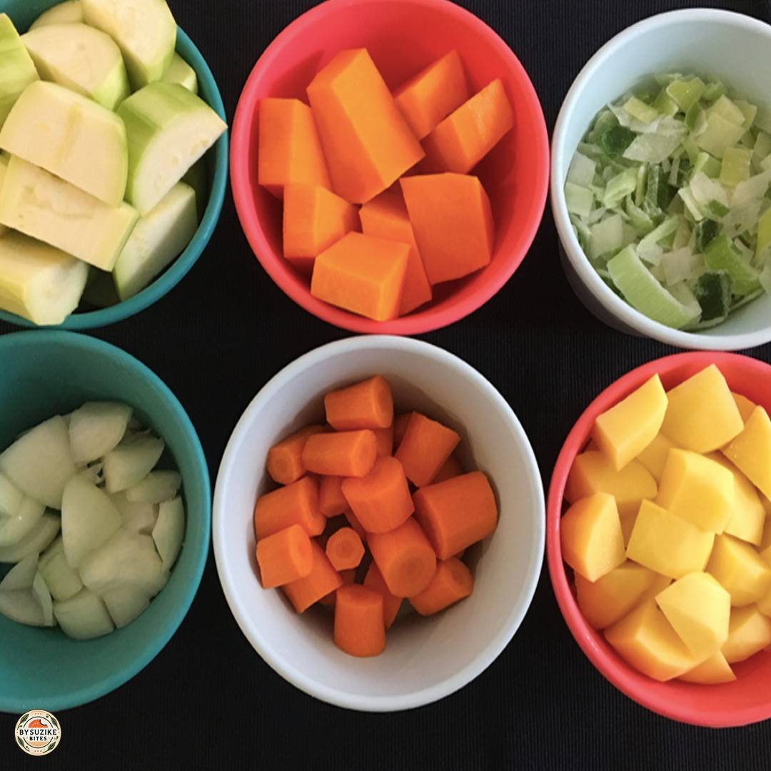 Creamy vegetable soup ingredients prepped in bowls (potato, pumpkin, zucchini, carrot, onion, leeks)