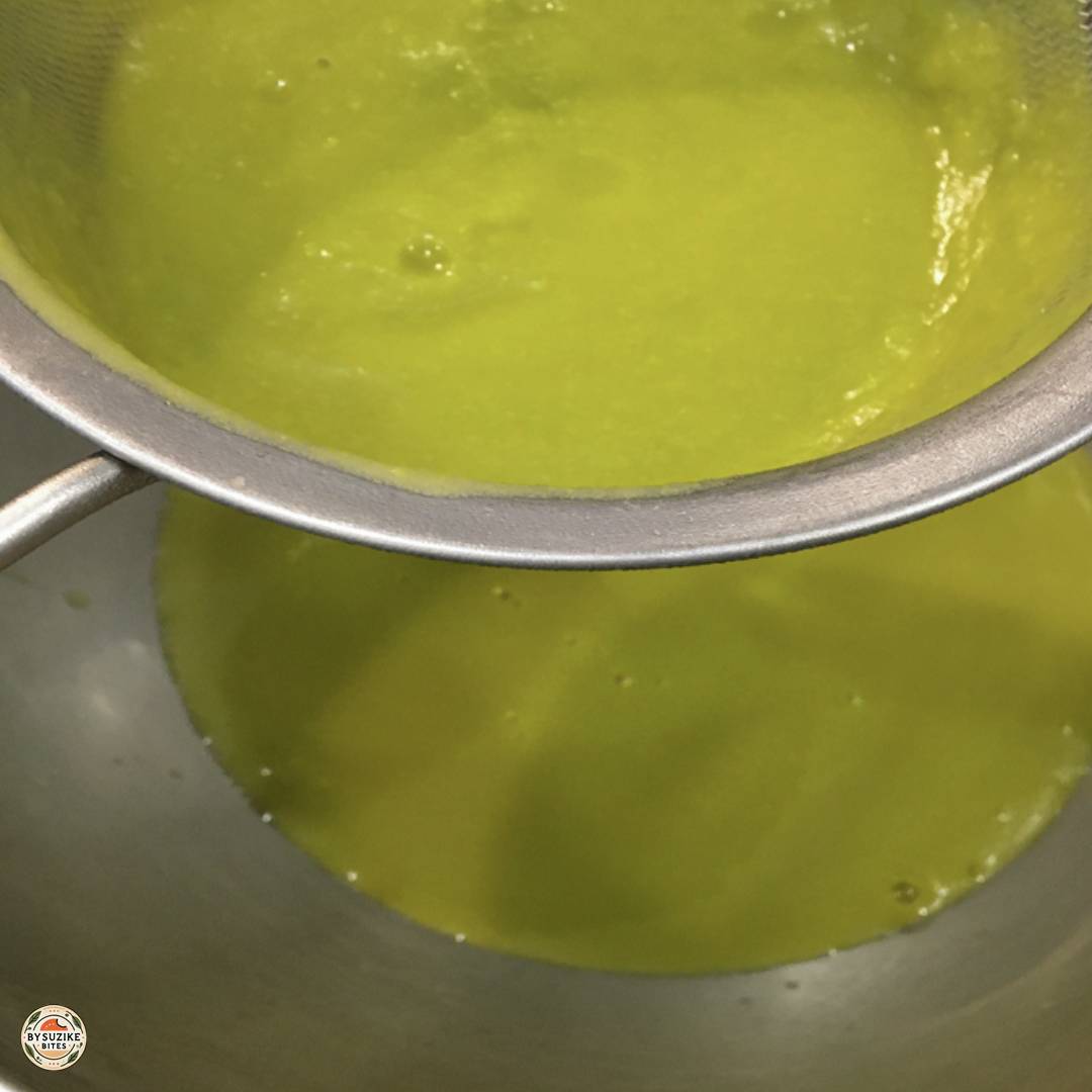Straining blended pea soup through a fine mesh sieve into a bowl.
