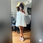 Beach outfit with summer hat featuring a white flowy dress, striped beach bag and light pink slides