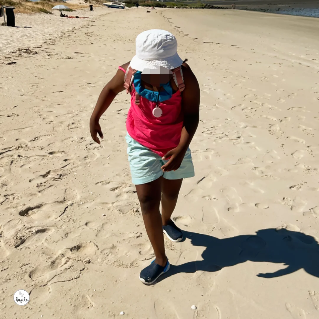 Child in a white sun hat walking across the sand at Praia Fluvial do Rosário.