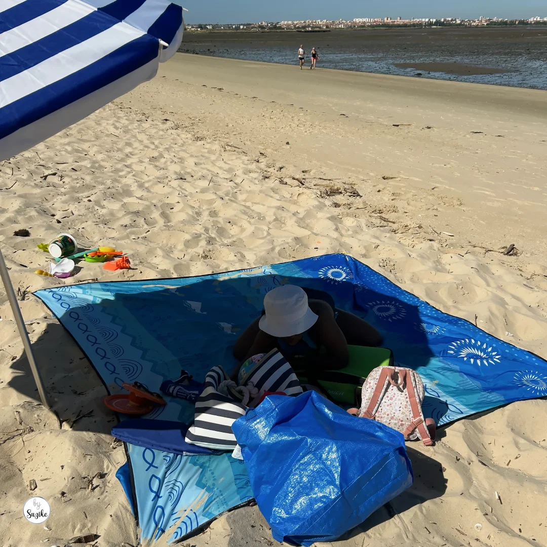 Blue beach blanket, umbrella, toys and family bags set up on the sand at Praia Fluvial do Rosário.