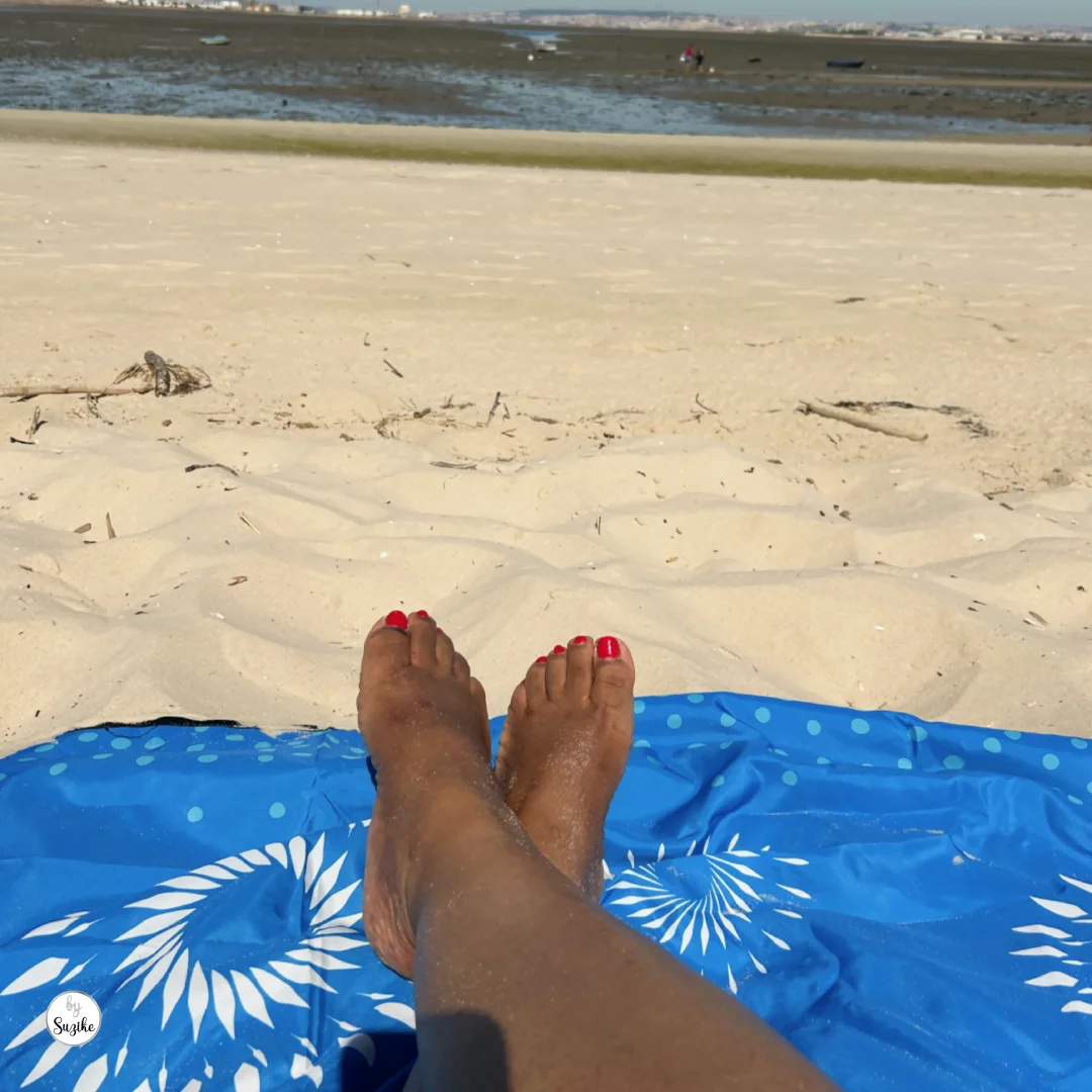 Woman smiling with the low-tide shoreline of Praia Fluvial do Rosário behind her.